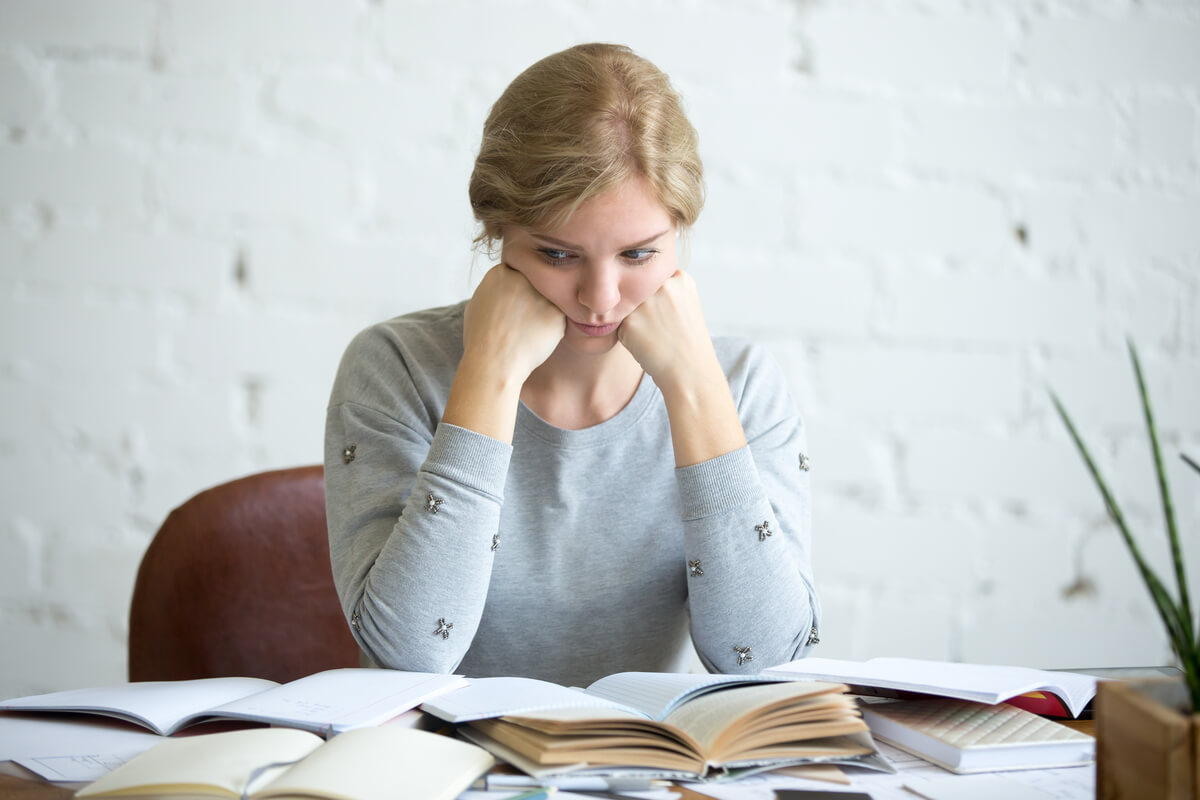 Jovem sentada com livros, pensando na ansiedade nos estudos.