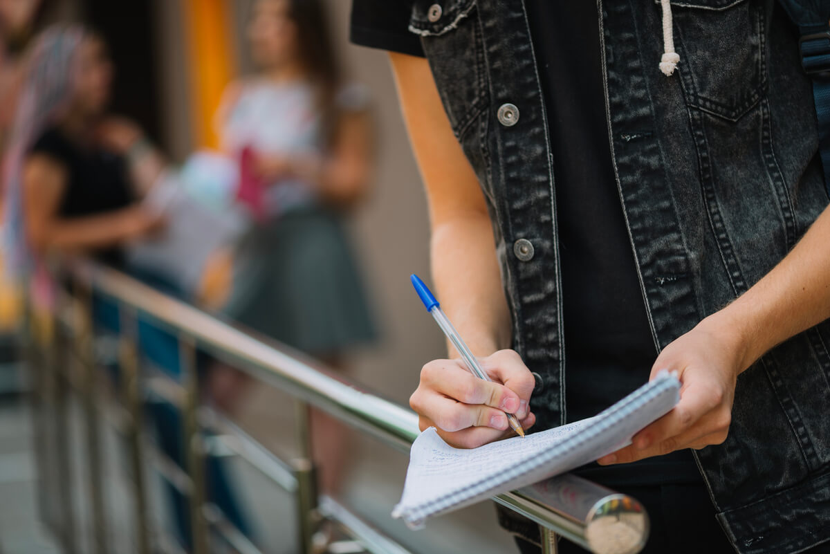 Jovem fazendo anotações sobre concurso público e faculdade em fila para o vestibular.