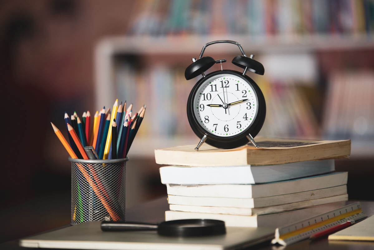 Relógio, lápis e livros em cima de uma mesa para estudos com a técnica de pomodoro.