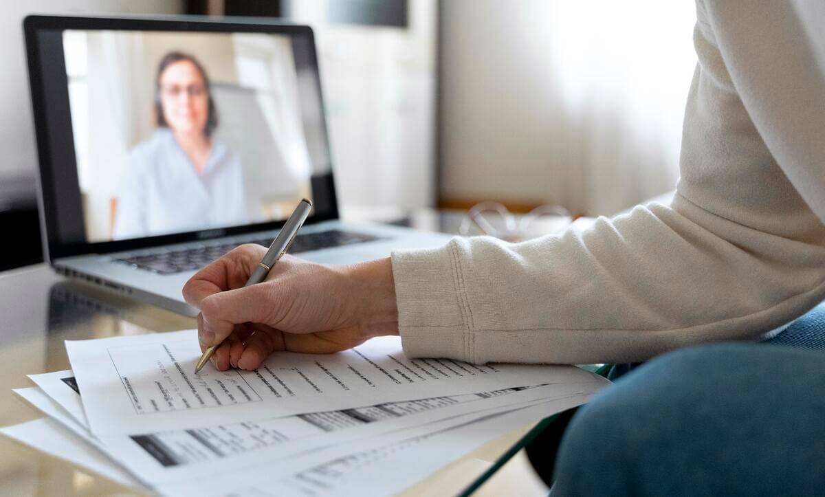 Jovem fazendo exercícios de Inglês enquanto escuta a professora no computador, por meio de uma educação personalizada.